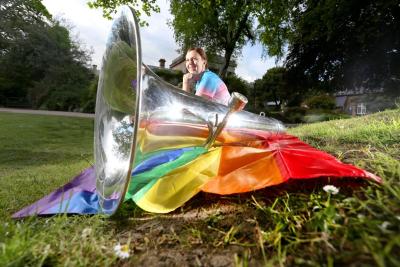 Women sits behind pride flag and brass instrument