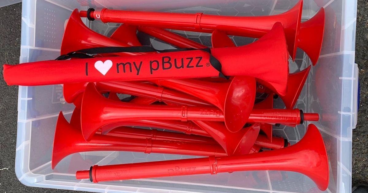 Pile of red pBuss'z in a plastic box. One says 'I love my pBuzz' on it