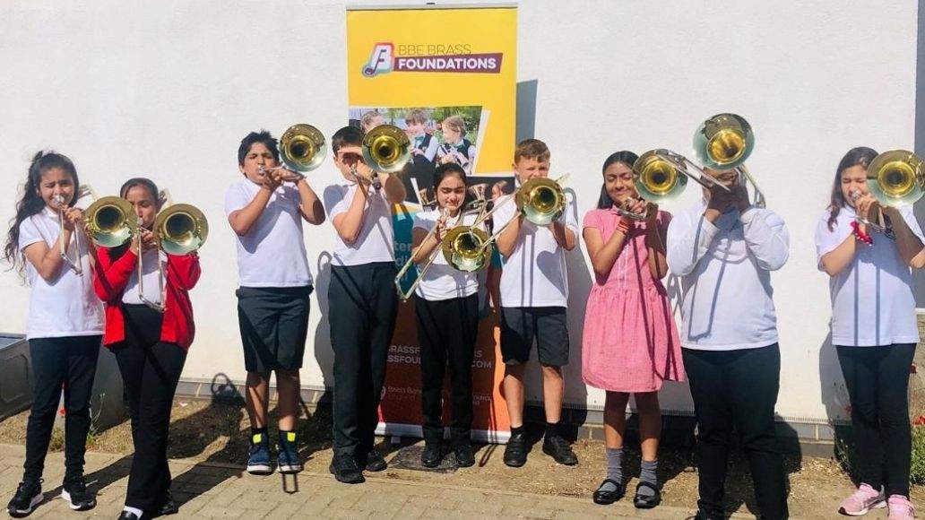 Line of children holding brass instruments, standing in front of a yellow Brass Foundations banner