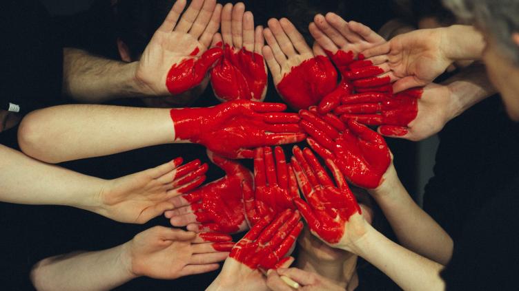 Many red painted hands placed together to form a heart shape