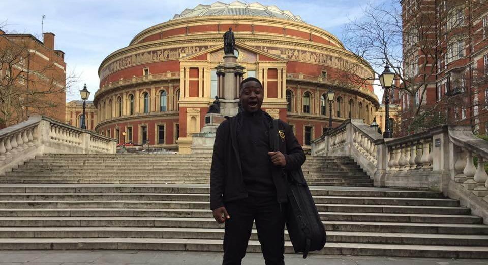 Ronald smiling widely standing on steps in front of Royal Albert Hall holding an instrument case