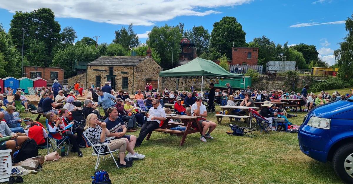 An audience enjoys listening to brass bands while seated in the sun at an event in 2022.