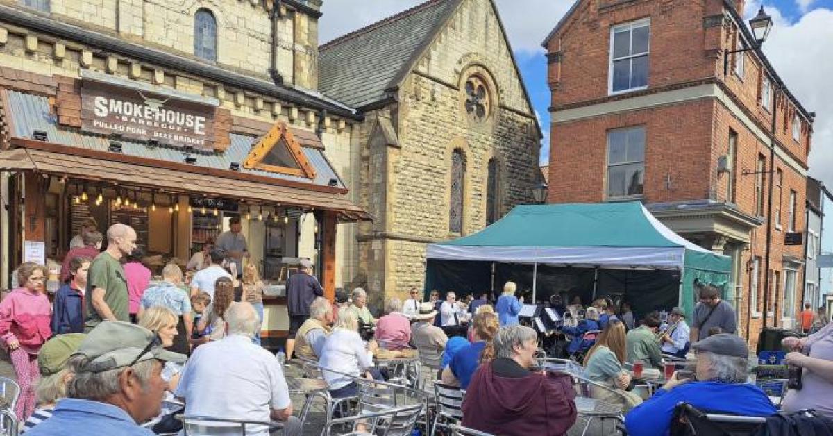 Outside at a food market in the middle of town. People are sitting around tables.