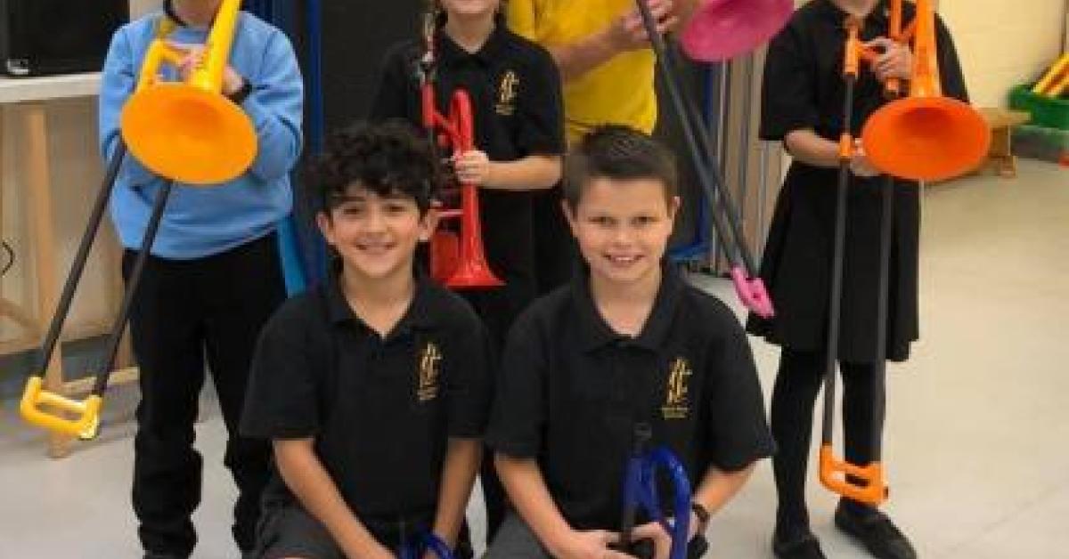 A group of primary school aged children holding brass instruments and smiling at the camera.