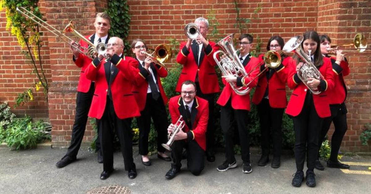 The band posing with their brass instuments wearing red jackets and black trousers.