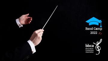 A male conductor's hands holding a baton, he is wearing a black jacket and a white shirt