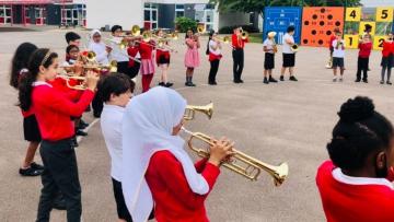 Children standing in a circle in a school tarmacked playground all playing a brass instrument