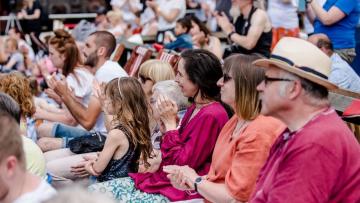 Adults and children sitting down facing forwards and clapping