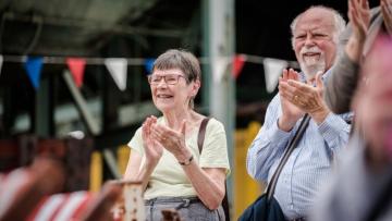 Man and woman are clapping they are standing in front of a string of coloured bunting