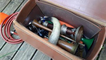 A brown leather case containing a selection of different shaped horns and a garden hose
