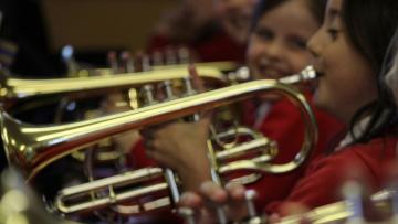 Close up of three children each playing a cornet, they are each wearing a red jumper