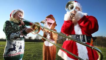 Three youth brass players are dressed in Christmas outfits holding their instruments
