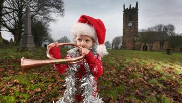 A child dressed up for Christmas plays a brass instrument