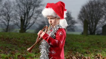 Child playing a brass instrument in a red jumper and Santa hat