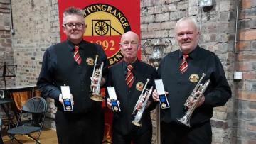 BBE CEO Kenny Crookston (far-left) stands with two members of his band. He holds his medal up to the camera