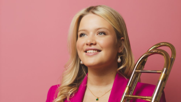 Award-winning trombonist Isobel Daws poses for the camera. She has mid-length blonde hair and wears a hot pink suit.