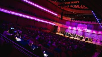 Audience in large dark hall with purple light emanating from stage