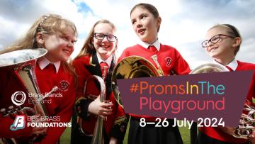 Group of four primary-school aged girls wearing red sweatshirts stood looking at each other in field holding brass instruments and smiling