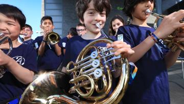 Group of young boys wearing navy blue t-shirts, the middle one is playing a french horn