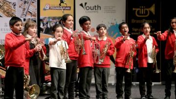 Line of children wearing red tops and holding cornets are holding their hands out towards the camera