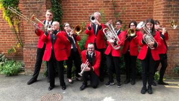 The band posing with their brass instuments wearing red jackets and black trousers.
