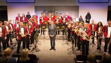 Amersham Band members are stood in a circle around their conductor, holding their instruments. They are wearing red blazers.