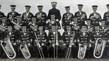 Old black and white photo of the band posing in ribboned uniforms with their instruments