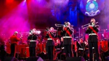 Line of marines standing on stage in uniform playing the trombone under a wash of pink and blue light
