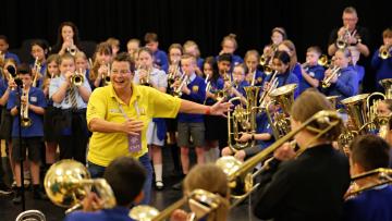 Helen smiling, interacting with a large group of young children playing brass instruments at Youth Fest 2024.