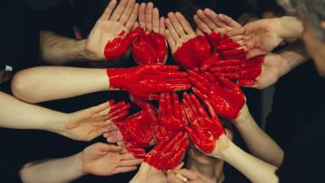 multiple hands put together to form a red heart 