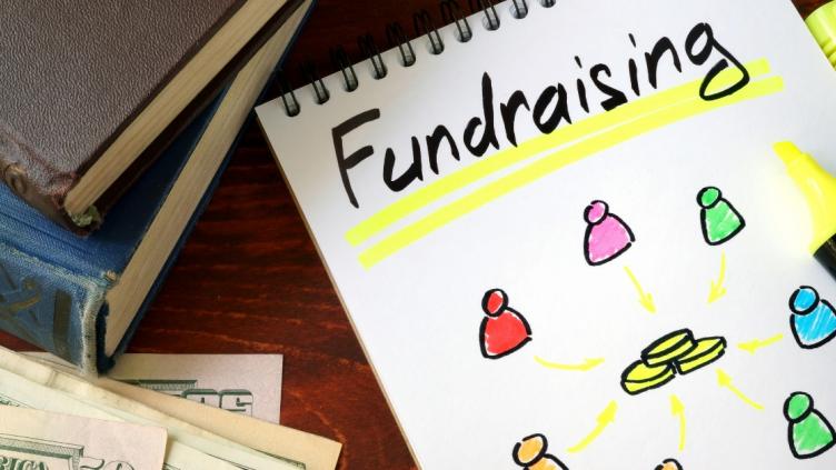 Fundraising is written on a white notepad where various cartoon figures are pointing towards a pile of coins