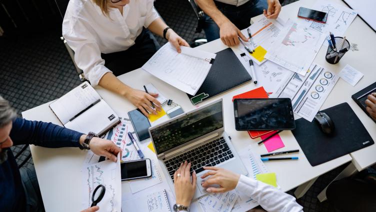 Large white desk with laptops, scattered bits of paper and pens