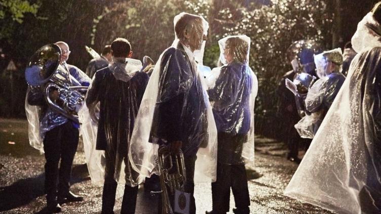 Group of musicians standing in the rain at dusk, wearing transparent rain ponchos