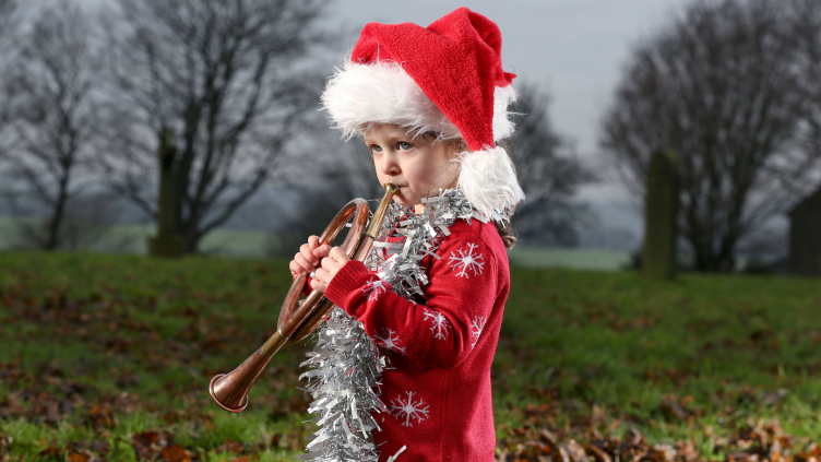 Child playing a brass instrument in a red jumper and Santa hat