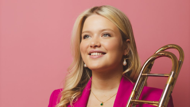 Award-winning trombonist Isobel Daws poses for the camera. She has mid-length blonde hair and wears a hot pink suit.