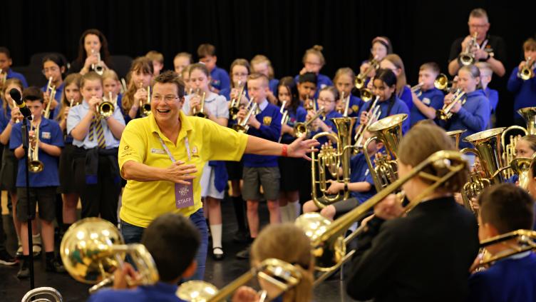Helen smiling, interacting with a large group of young children playing brass instruments at Youth Fest 2024.