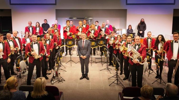 Amersham Band members are stood in a circle around their conductor, holding their instruments. They are wearing red blazers.