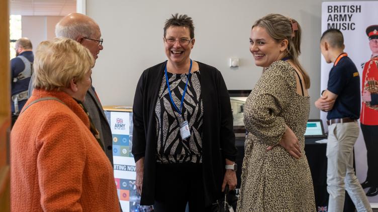 Three women and a man stand together, women in the middle smiles at the camera