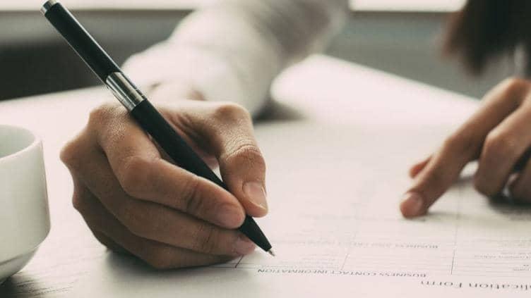 Hand holding a pen, leaning on a piece of white paper ready to write