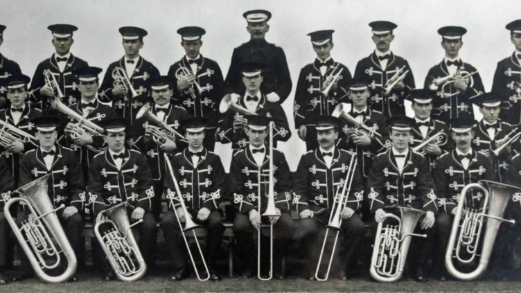 Old black and white photo of the band posing in ribboned uniforms with their instruments