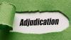 A piece of green paper has been ripped and pulled out to reveal the word Adjudication written in black on white